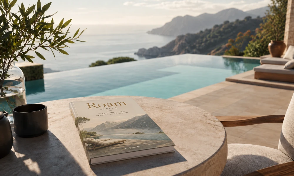 Roam Annual Volume 01 resting on a marble table beside an infinity pool overlooking the Mediterranean coast