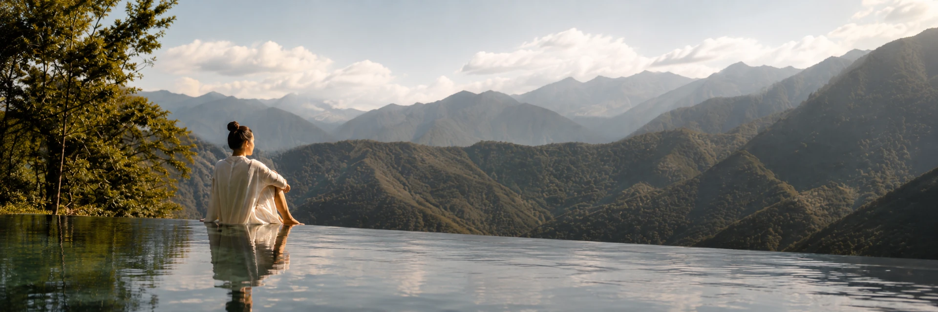 A woman sitting at the edge of an infinity pool looking out over forested mountains